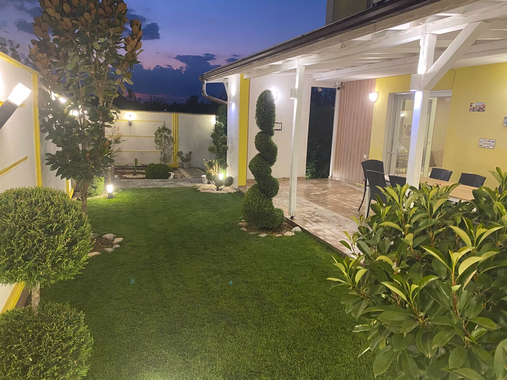 Jardín nocturno con topiarios y pérgola iluminada