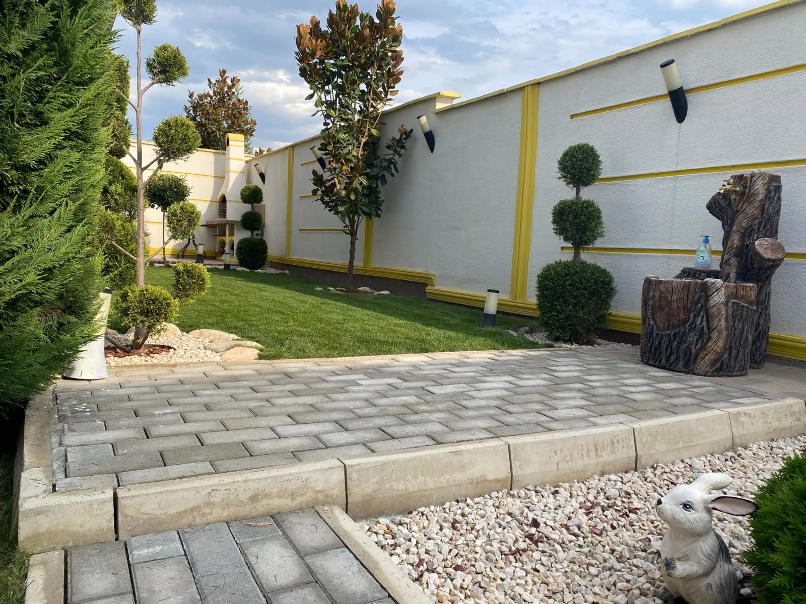 Patio con topiarios y césped junto a un muro blanco